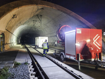 Ein Großventilator steht bei Nacht am Beginn eines Eisenbahntunnels. 