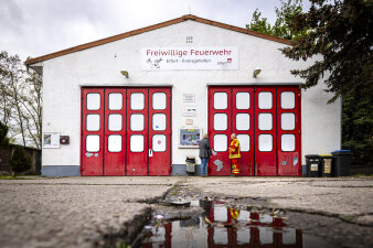 Vor einem Feuerwehrgebäude stehen zwei Männer, eine in zivil und einer in Feuerwehruniform. 