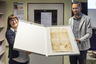 ein Mann und eine Frau halten in einem großen Pappkarton eine historische Pergamenturkunde