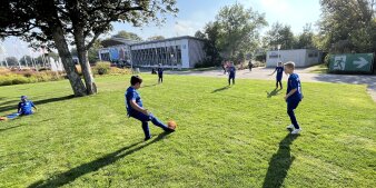 Kinder in Fußballtrikots spielen auf einer Wiese. 