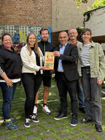 Menschen stehen vor einer Wand und bekommen einen Pokal aus Holz überreicht