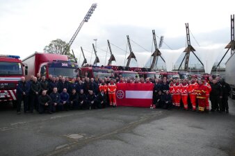 Viele Menschen in Uniform stehen vor Feuerwehrautos und zeigen eine große Flagge mit den Stadtsymbolen von Erfurt. 