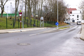 Eine aspahaltierte Straße führt durch einen Ort, im Hintergrund fährt ein PKW