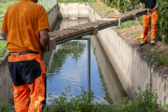 zwei Männer heben einen Holzsteg in ein mit Wasser gefülltes Betonbecken
