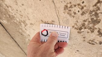 Eine Hand hält eine Messkarte an einen Riss in einer Betonfläche