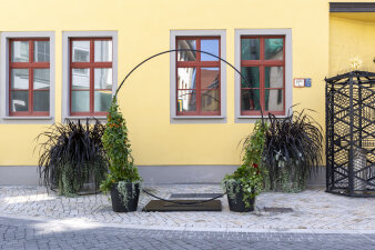 bepflanzter Metallring vor gelber Hausfassade