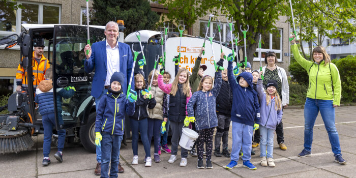 mehrere Kinder und drei Erwachsene mit Müllgreifern vor einem Kehrfahrzeug