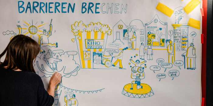 eine Person steht vor einer beschrifteten Papierbahn, darauf die Überschrift "Barrieren brechen"