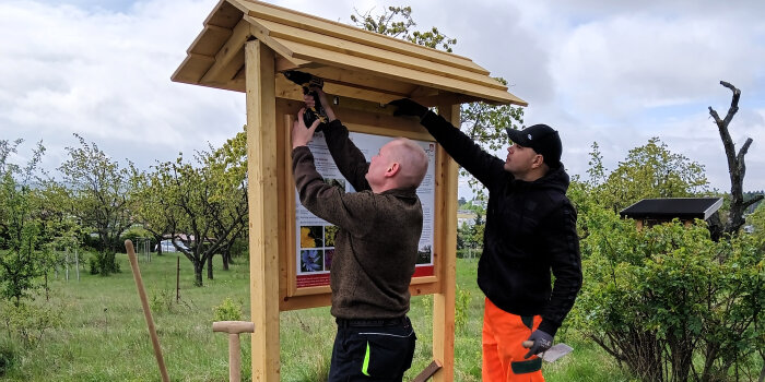 Zwei Männer bauen mit Werkzeug die Infotafel auf