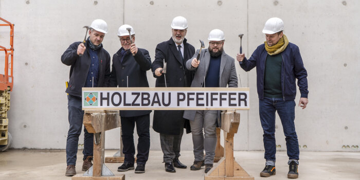 fünf Männer hämmern große Nägel in einen Holzbalken