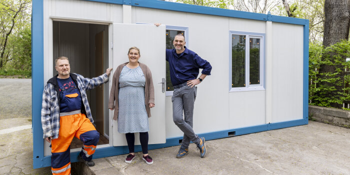 drei Personen stehen vor einem weiß-blauen Container