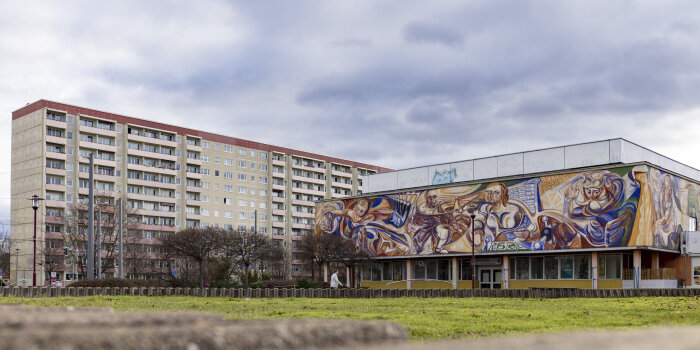 ein Gebäude in DDR-Architektur mit Wandbild, daher ein mehrgeschossiges Haus in Plattenbauweise
