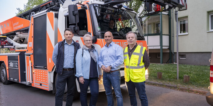 vier Personen stehen vor einem Feuerwehrfahrzeug