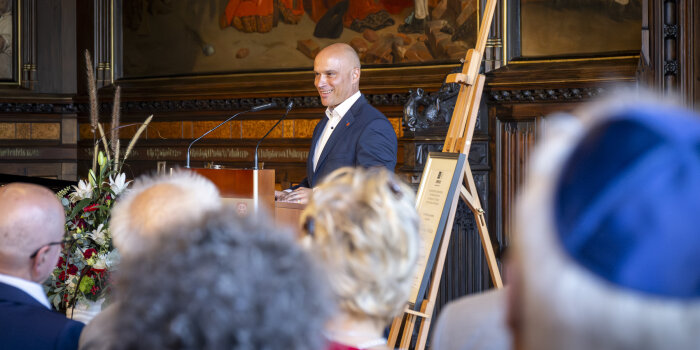 Foto: Oberbürgermeister Andreas Horn hält Rede zur Übergabe der Unseco-Urkunde 11.8.2024 © Stadtverwaltung Erfurt Mann hält Rede an Pult vor Menschen mit Staffelei und Urkunde neben sich.