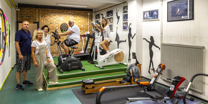 Zwei Männer, zwei Frauen und ein Mädchen sind in einem Fitnessraum. Das Mädchen und ein Mann nutzen die Geräte. 