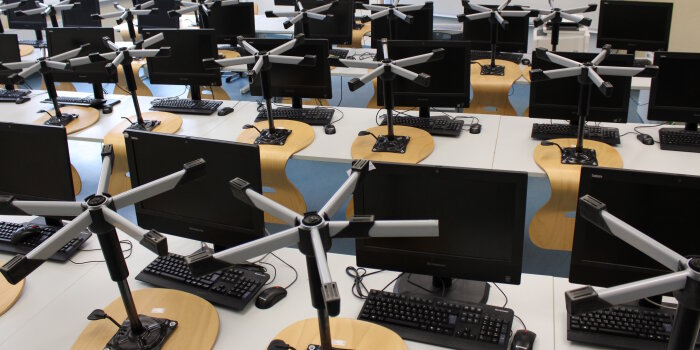 In einem Klassenzimmer stehen Computer und auf den Tischen sind Drehstühle hochgestellt.