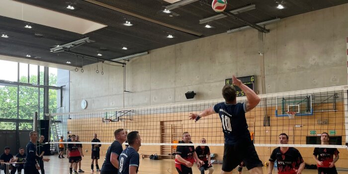 Zwei Männermannschaften spielen Volleyball gegeneinander. Ein Spieler setzt zum Schmetterball an.