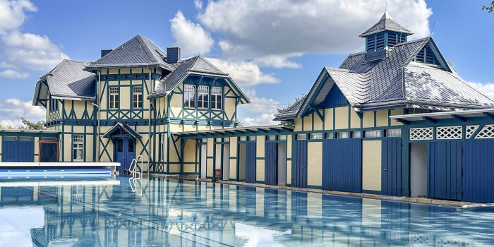 Ein Schwimmbecken. Im Hintergrund stehen sanierte Fachwerkhäuser.