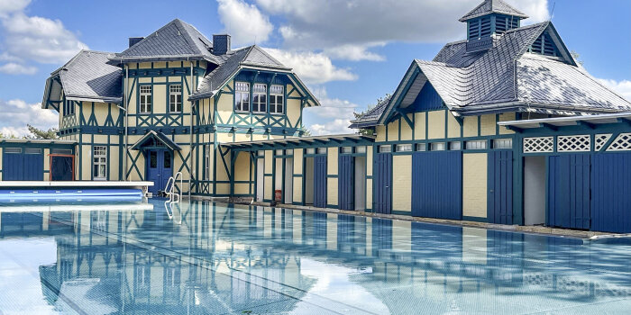 Ein Schwimmbecken. Im Hintergrund stehen sanierte Fachwerkhäuser.