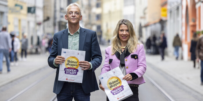ein Mann und eine Frau halten Papiertüten mit Aufdruck "Heimat shoppen" in der Hand