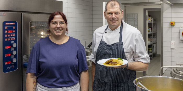 Ein Mann und eine Frau, beide mit Schürze, präsentieren einen Teller voll mit Bio-Kost. 