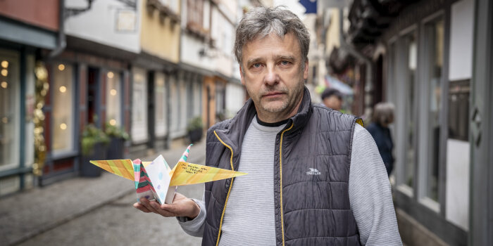 ein Mann hält einen gefalteten Kranich aus Papier in der Hand