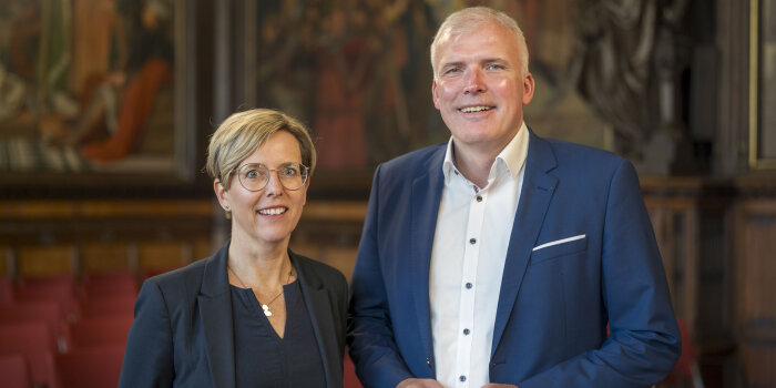 eine Frau mit kurzen Haaren und Brille und ein Mann im blauen Sakko