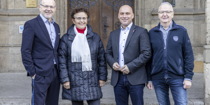Drei Männer und eine Frau, alle dunkelblau gekleidet, stehen nebeneinander. 