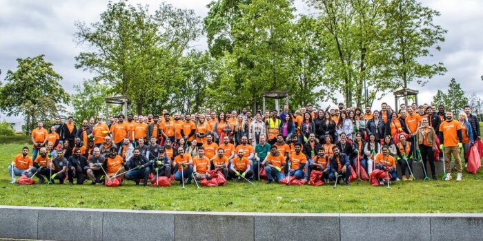 Viele Männer und Frauen stehen für ein Gruppenfoto auf einer Grünfläche und halten Müllsäcke und Müllgreifer.