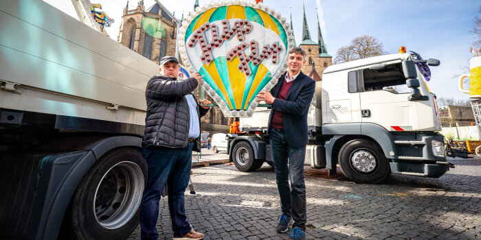 Zwei Männer stehen auf einem Rummelplatz und berühren ein Bauteil mit der Aufschrift "Flip Fly".