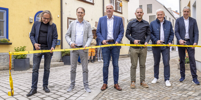 sechs Männer schneiden ein gelbes Band durch