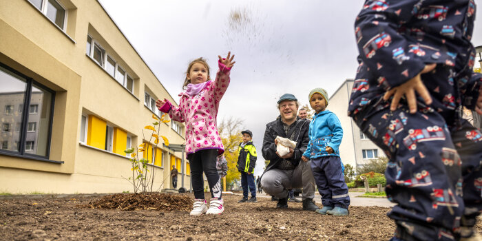 Ein Mann kniet am Boden ringsherum Kinder, alle bringen Saatgut ein