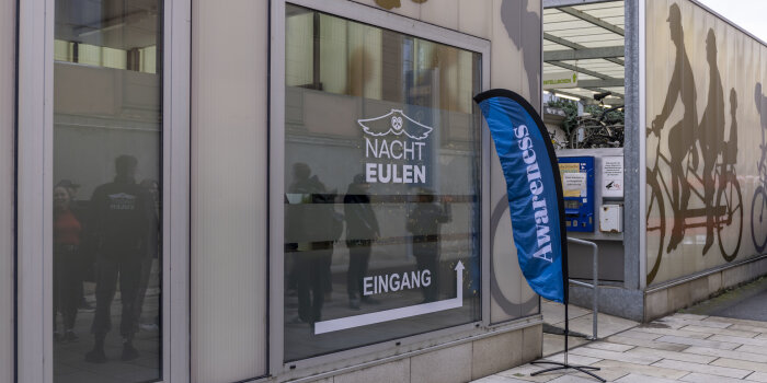 Außenansicht eines Gebäudes mit großem Fenster, das ein Logo "Nachteulen" trägt