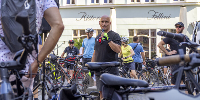 Ein Mann spricht in ein Mikrofon, um ihn herum stehen Radfahrer