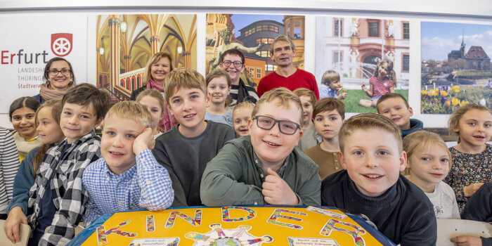 Drei Frauen, ein Mann und viele Kinder stehen hinter einem Koffer. Auf dem Koffer steht „Kinderrechte“. 