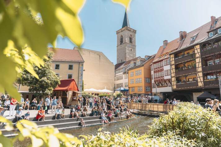 eine bebaute Brücke, davor viele Menschen und einige Zelte