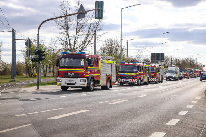 Mehrere Feuerwehrfahrzeuge fahren in Kolonne eine Straße entlang. 