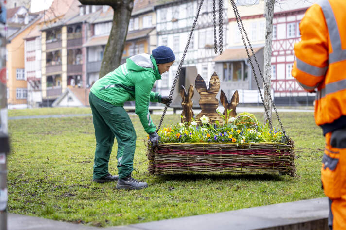 ein kleines Blumenbeet mit Osterdeko wird an einem Haken auf eine Grünfläche gehoben