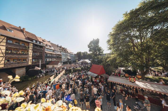 eine bebaute Brücke, davor viele Menschen und einige Zelte