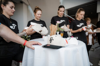 mehrere Frauen stehen an einem Stehtisch, auf dem eine Basecap mit den gestickten Buchstaben E und F liegt