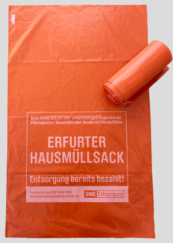 Ein orangefarbener Müllsack mit Aufdruck, darauf liegt eine Rolle gleicher Müllsäcke
