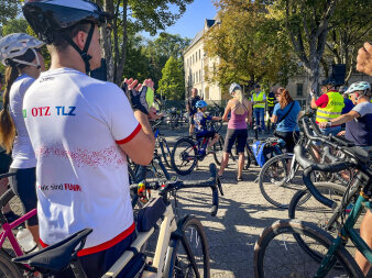 zahlreiche Radfahrer stehen auf einem städtischen Platz; ein Mann spricht in ein Mikrofon