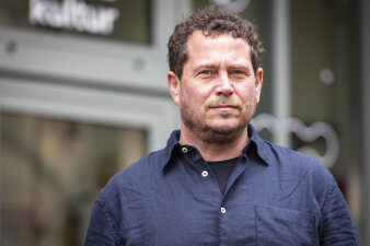 ein Mann mit kurzen lockigen Haaren, kurzem Bart und dunkelblauem Hemd