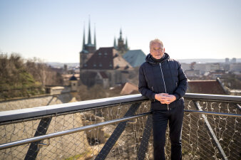 ein schwarz gekleideter Mann steht auf der Mauerkronenbrücke, im Hintergrund der Erfurter Dom mit Severikirche