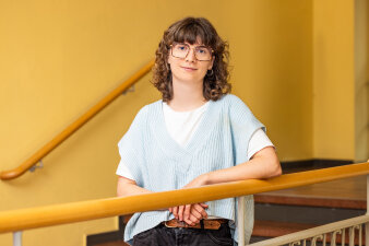 Eine junge Frau mit Brille und krausem Haar lehnt auf einem Treppengeländer.