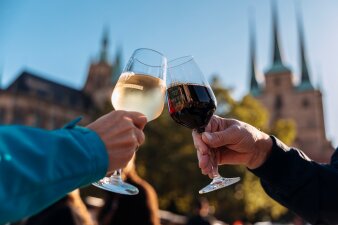 zwei Hände stoßen mit je einem Glas Weißwein und einem Glas Rotwein an