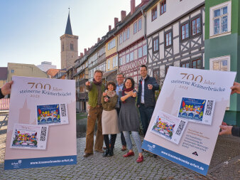 zwischen zwei Plakaten, auf denen Briefmarken abgebildet sind, stehen fünf Personen
