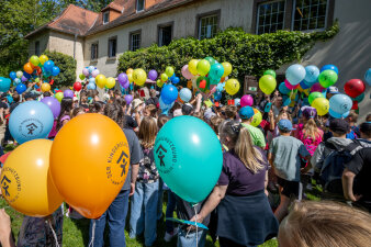 Erwachsene und Kinder halten viele bunte Luftballons in der Hand.