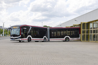 ein Gelenkbusse fährt aus dem gelben Tor eines Gebäudes