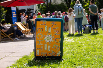 Ein Koffer mit Aufschrift „Kinderrechtekoffer“ steht auf einer Wiese. 
